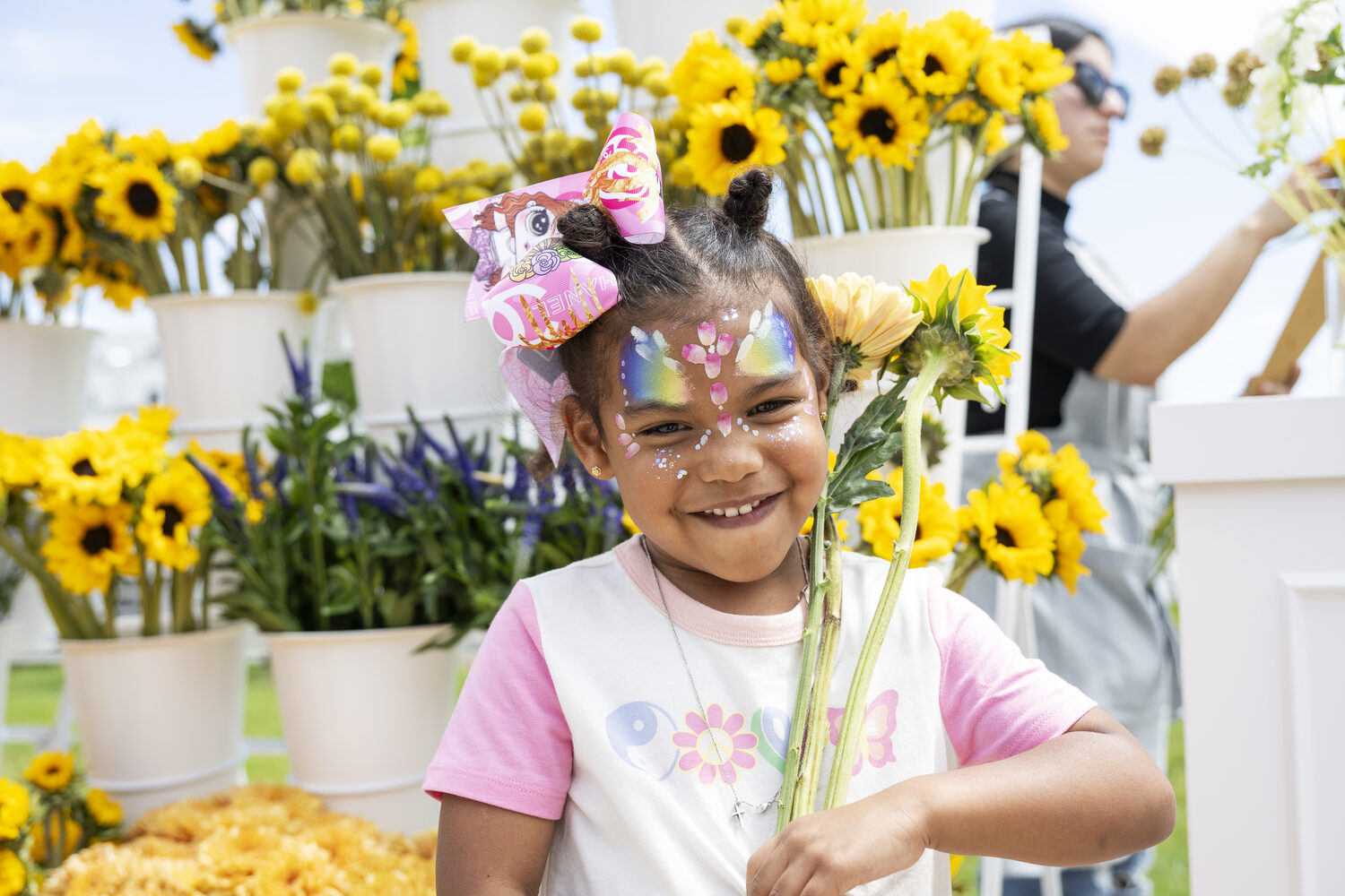 A child with face paint holding sunflowers